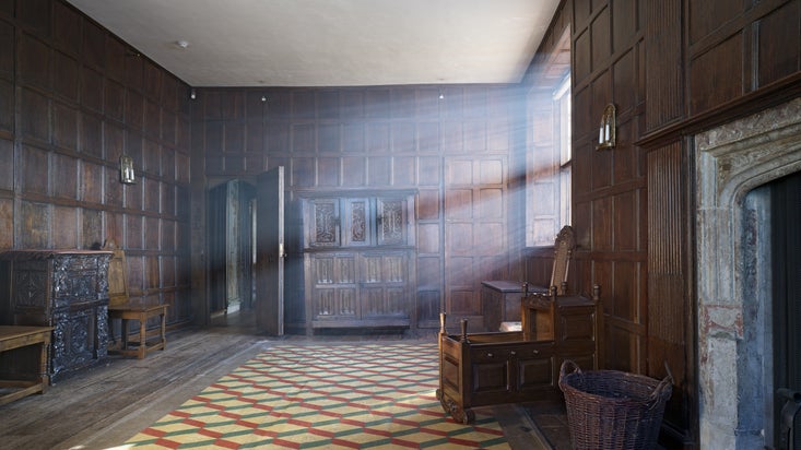 A wooden panelled room in a Tudor house with sunlight streaming through the windows onto a geometric floor.